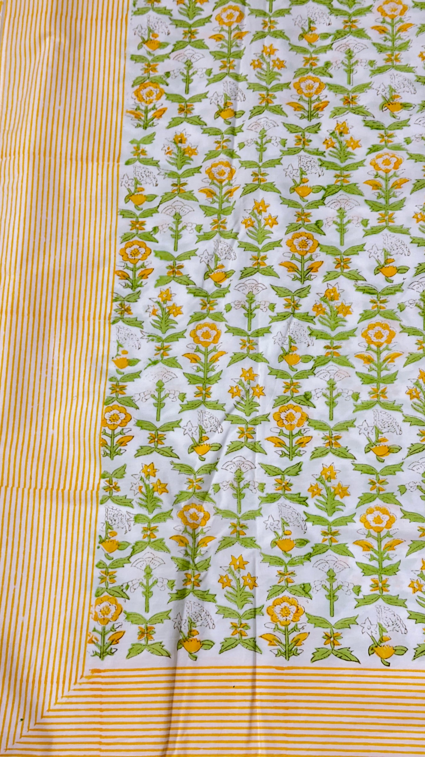 A close-up of a printed fabric panel with a white base, repeating yellow and green floral motifs, and a striped yellow border.